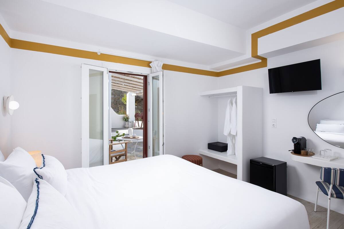 Habitación de hotel con cama, escritorio con televisor, refrigerador pequeño y baño con ducha e inodoro.