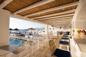 A poolside area with seating and tables, overlooking a pool and a scenic view of mountains.