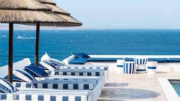 Zona de piscina con sillones de descanso y sombrillas, con vista al océano.