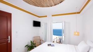 Un dormitorio con cama, televisión, silla, mesita y vista al mar.