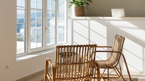 Una habitación con un amplio ventanal arqueado, un ordenador portátil sobre una estantería y dos sillones de mimbre.