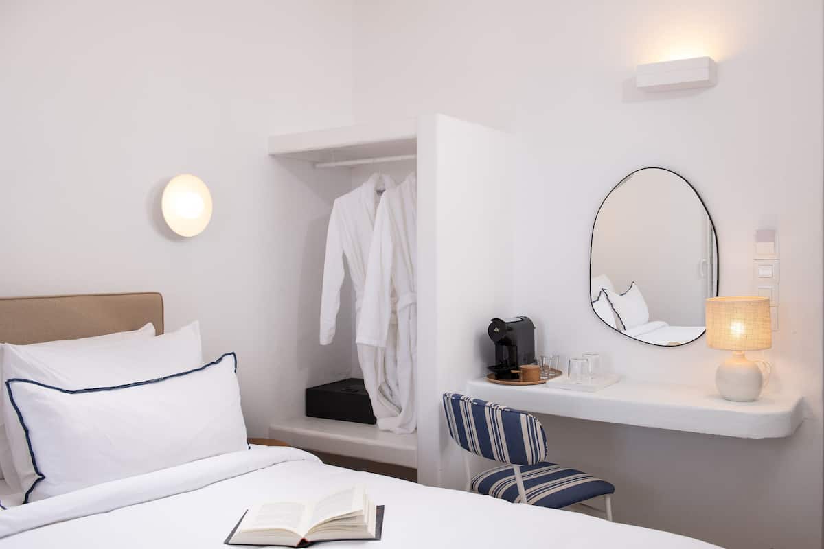 Habitación de hotel con cama, mesita de noche con lámpara, una silla, bata colgada y espejo.