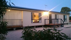 A single-story mobile home with a porch, a small deck, and a visible interior with a bed and a window.