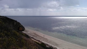 A coastal beach with a rocky cliff and a person walking along the shore.