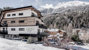 Un hotel moderno con fachada de madera, varios balcones y vistas a montañas nevadas.