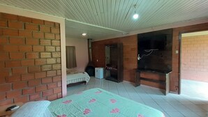 A room with a brick wall, a bed with a floral bedspread, a small table with a remote control, and a fireplace.