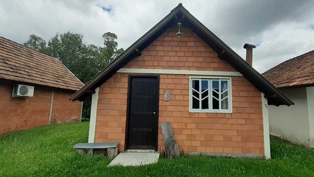 Una pequeña casa de ladrillo con puerta negra, ventana de marco blanco y un banco pequeño al frente.