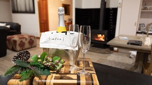 A bottle of champagne with a tag labeled "stir" on a wooden tray, accompanied by two glasses, in a living room setting with a fireplace. - Bare Foot Luxury, minutes from Maleny Town Centre (Maleny)
