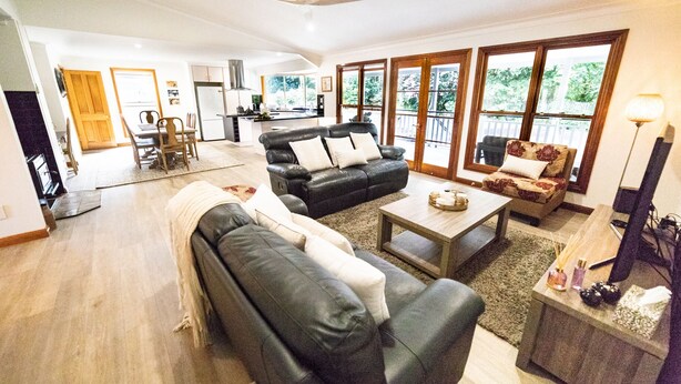 A spacious living room with a black leather sofa, a wooden coffee table, and a dining area with a wooden table and chairs. - Bare Foot Luxury, minutes from Maleny Town Centre (Maleny)
