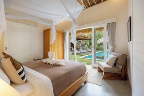 A bedroom with a bed, a sitting area with a chair, a large window, and a view of a pool and outdoor area.