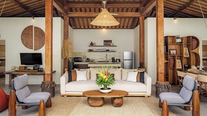 Un salon spacieux avec un canapé, des fauteuils, une table basse, un téléviseur et une cuisine en arrière-plan.