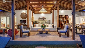 Un vaste espace de vie doté d’un haut plafond, un coin salon central avec un canapé et des fauteuils, une cuisine à l’arrière-plan et un coin repas avec une table et des chaises.