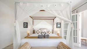 Ein Schlafzimmer mit einem Himmelsbett, zwei Nachttischlampen und einer Sitzbank am Fußende des Bettes.