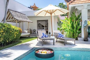Zona de piscina con sillas de descanso, una mesa de comedor y un espacio de estar cubierto.