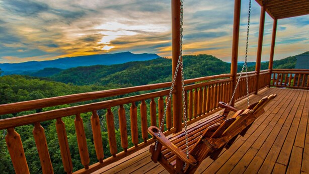 Une terrasse en bois avec un fauteuil suspendu, offrant une vue sur une chaîne de montagnes boisées.