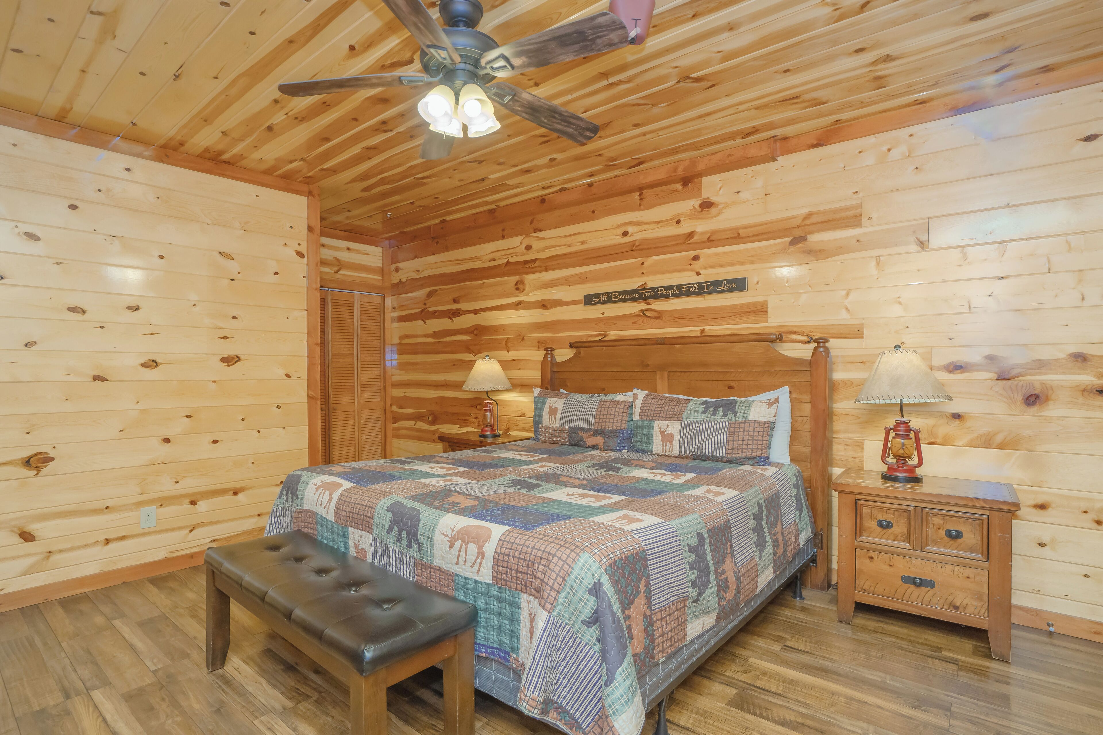 A wooden cabin bedroom with a bed, bench, nightstands, and a ceiling fan.