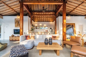 A spacious living area with a large sofa, a coffee table, and a dining area with a kitchen in the background.