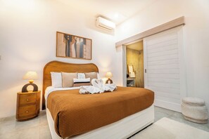 A neatly arranged bedroom with a bed, bedside tables, a wall-mounted air conditioner, and a door leading to another room. - Villa Thiara Oberoi Seminyak 500m Kudeta beach (Seminyak)