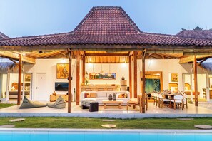 A two-story building with a tiled roof, a covered outdoor seating area, a pool, and a well-maintained lawn.
