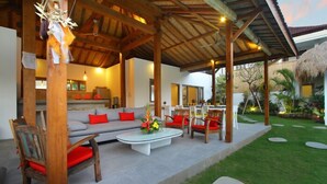 Eine überdachte Terrasse im Freien mit einer Couch, Sesseln und einem Couchtisch.