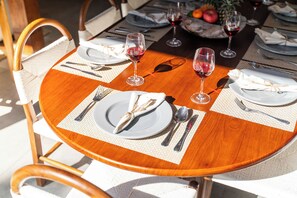 A round wooden dining table with white plates, silverware, and glasses of red wine. - Villa Thiara Oberoi Seminyak 500m Kudeta beach (Seminyak)