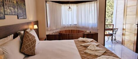 A hotel room with a large bed, a wooden bathtub, a balcony with a chair, and a chandelier.