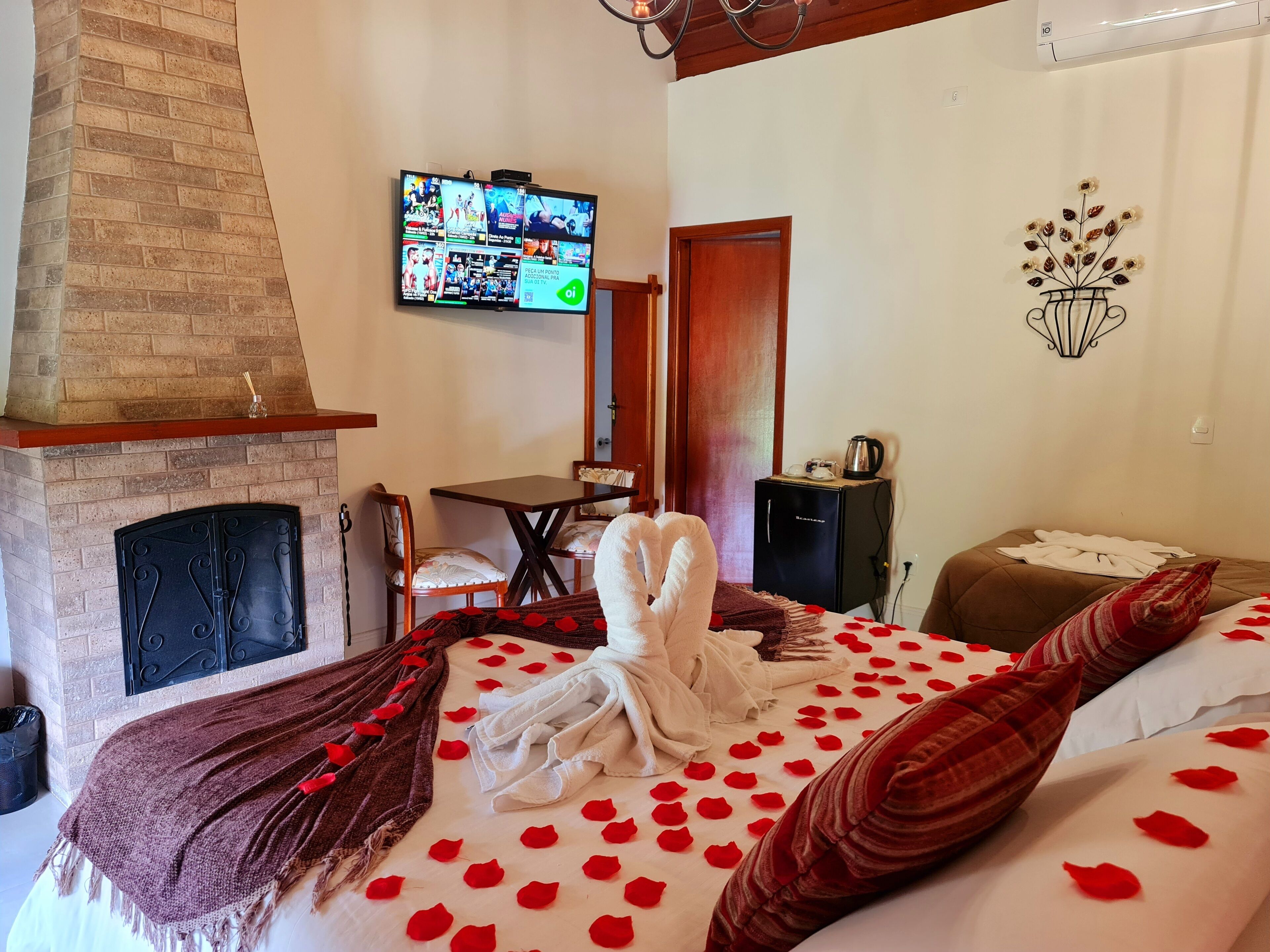 Ein Hotelzimmer mit Kamin, Wandfernseher, kleinem Tisch und einem Bett, das mit Rosenblättern dekoriert ist.