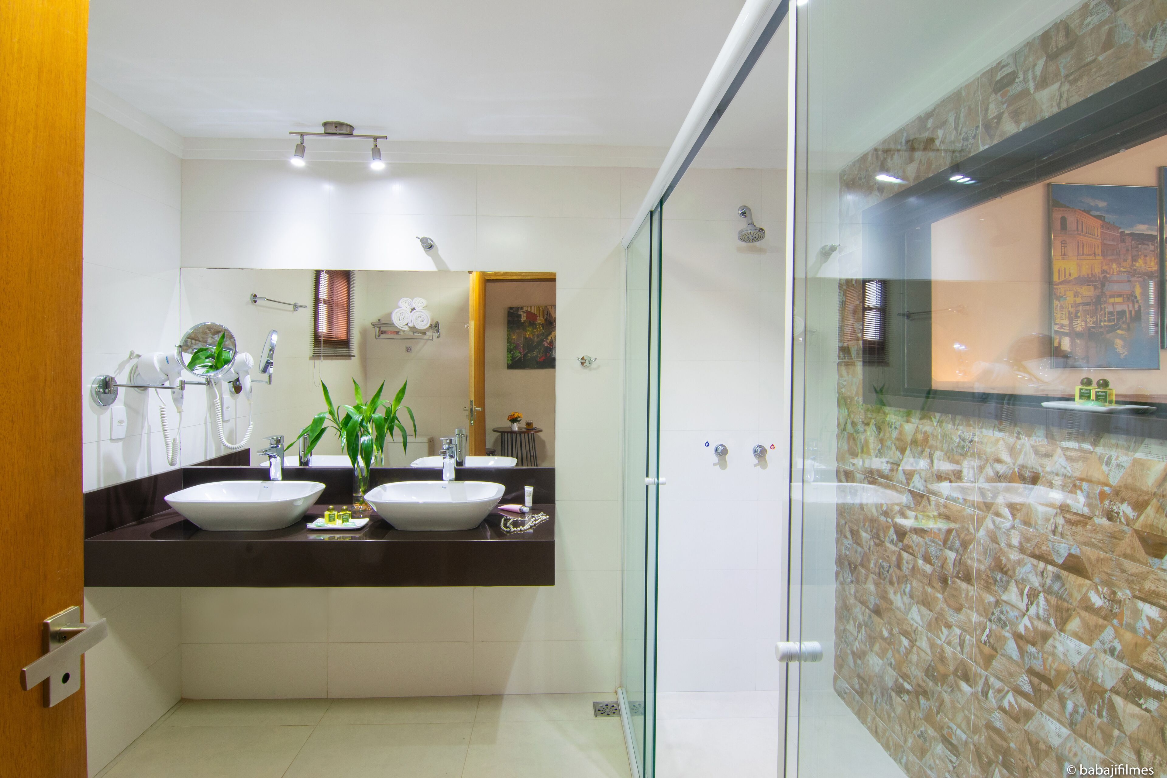 A modern bathroom with two sinks, a glass shower enclosure, and a stone wall.