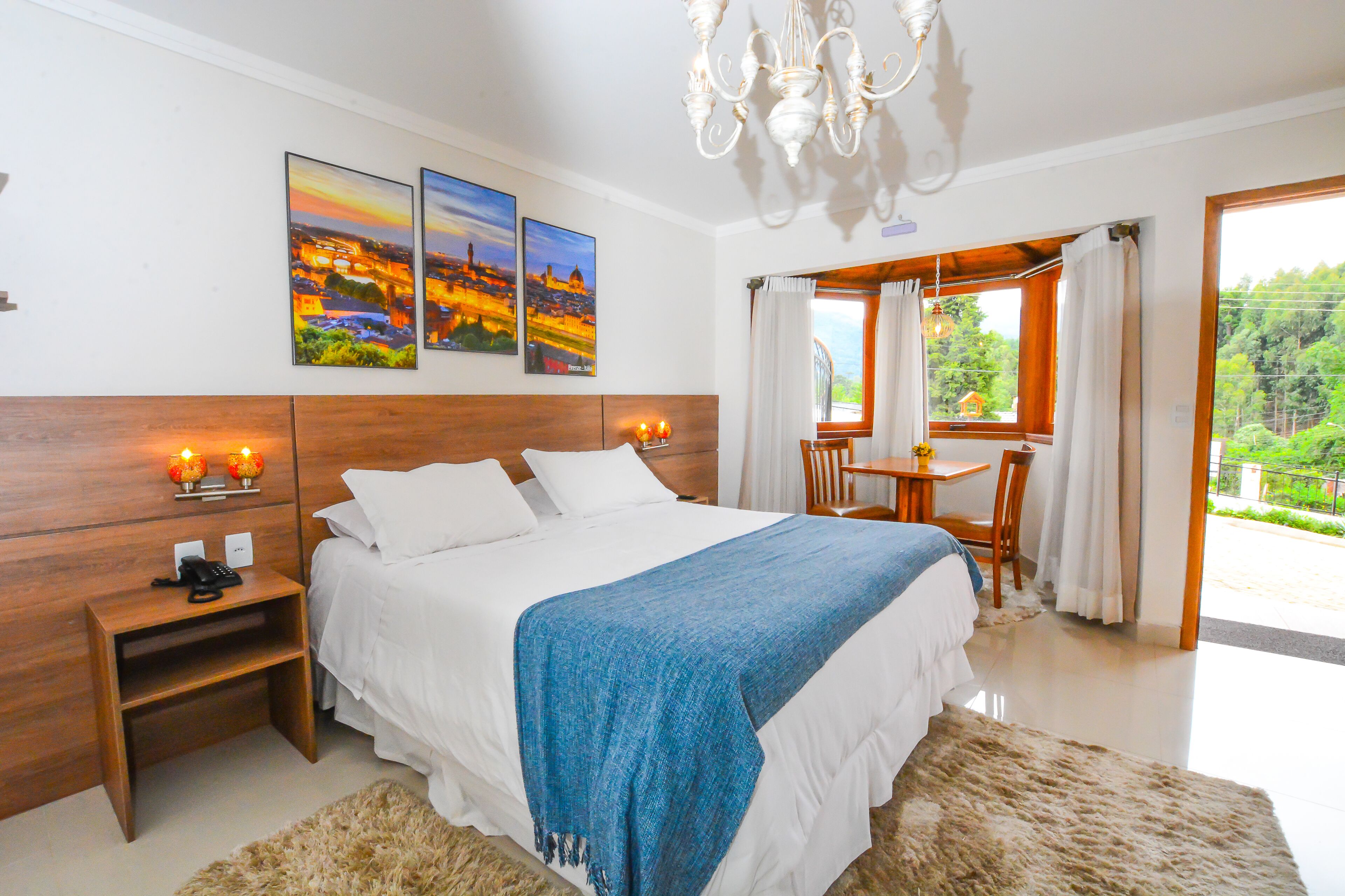 A bedroom with a large bed, a wooden headboard, a nightstand, a desk, and a view of the outdoors.