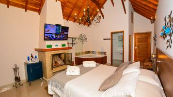 Un dormitorio con una cama grande, techo de madera, televisor montado en la pared y chimenea.