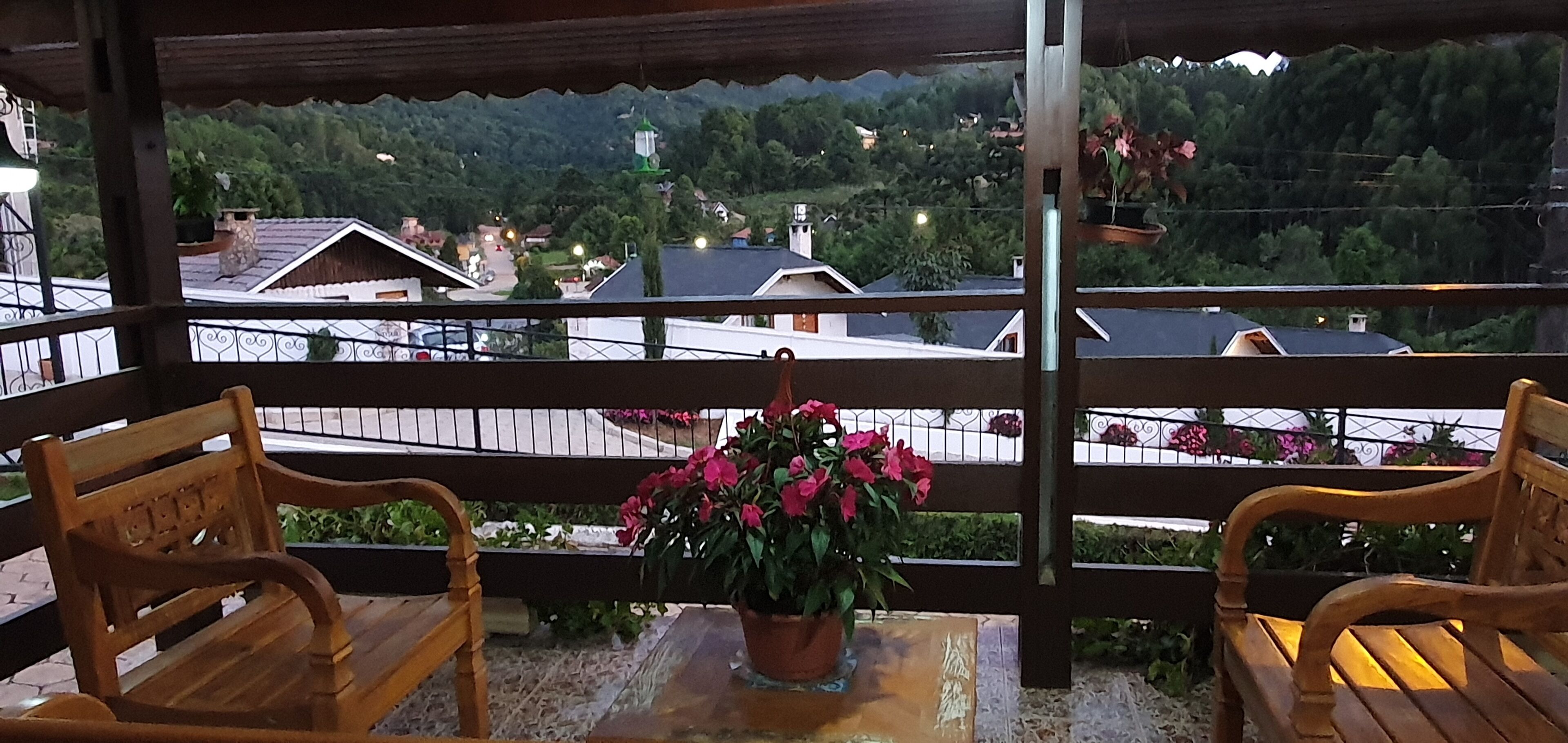 Eine Holzbank mit einem Blumentopf auf einem Balkon mit Blick auf ein Dorf mit Häusern und Grünflächen.
