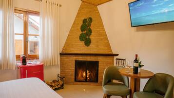 A room with a fireplace, a bed, a TV, and two chairs.