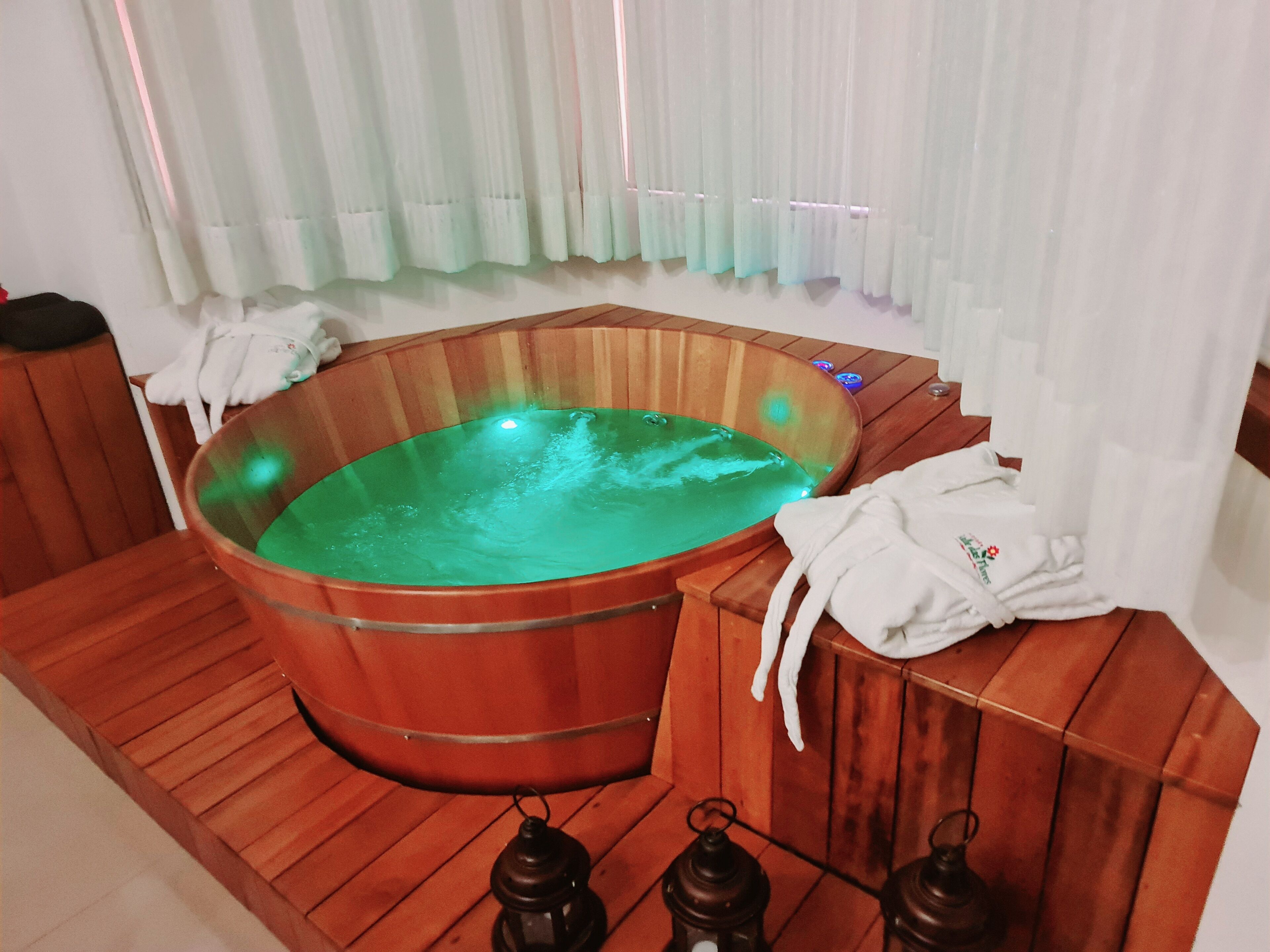 Un bain à remous en bois, avec une fontaine dont l’eau a une teinte verdâtre, entouré d’un sol en bois et de serviettes blanches.