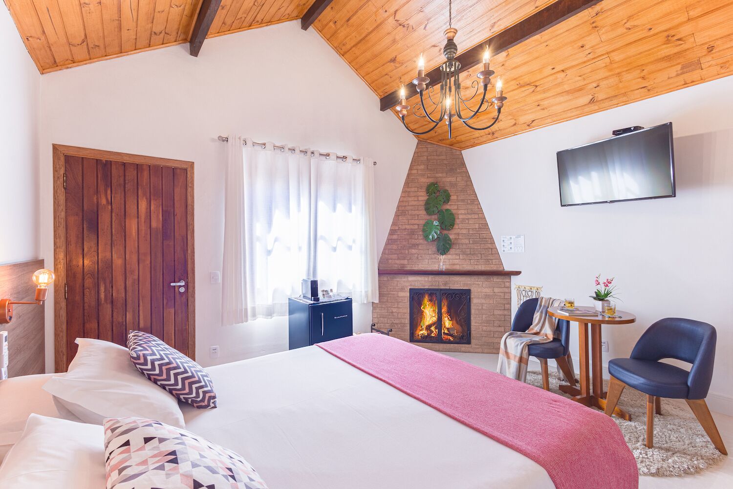 Un dormitorio con una cama grande, chimenea, televisor y una pequeña mesa con sillas.