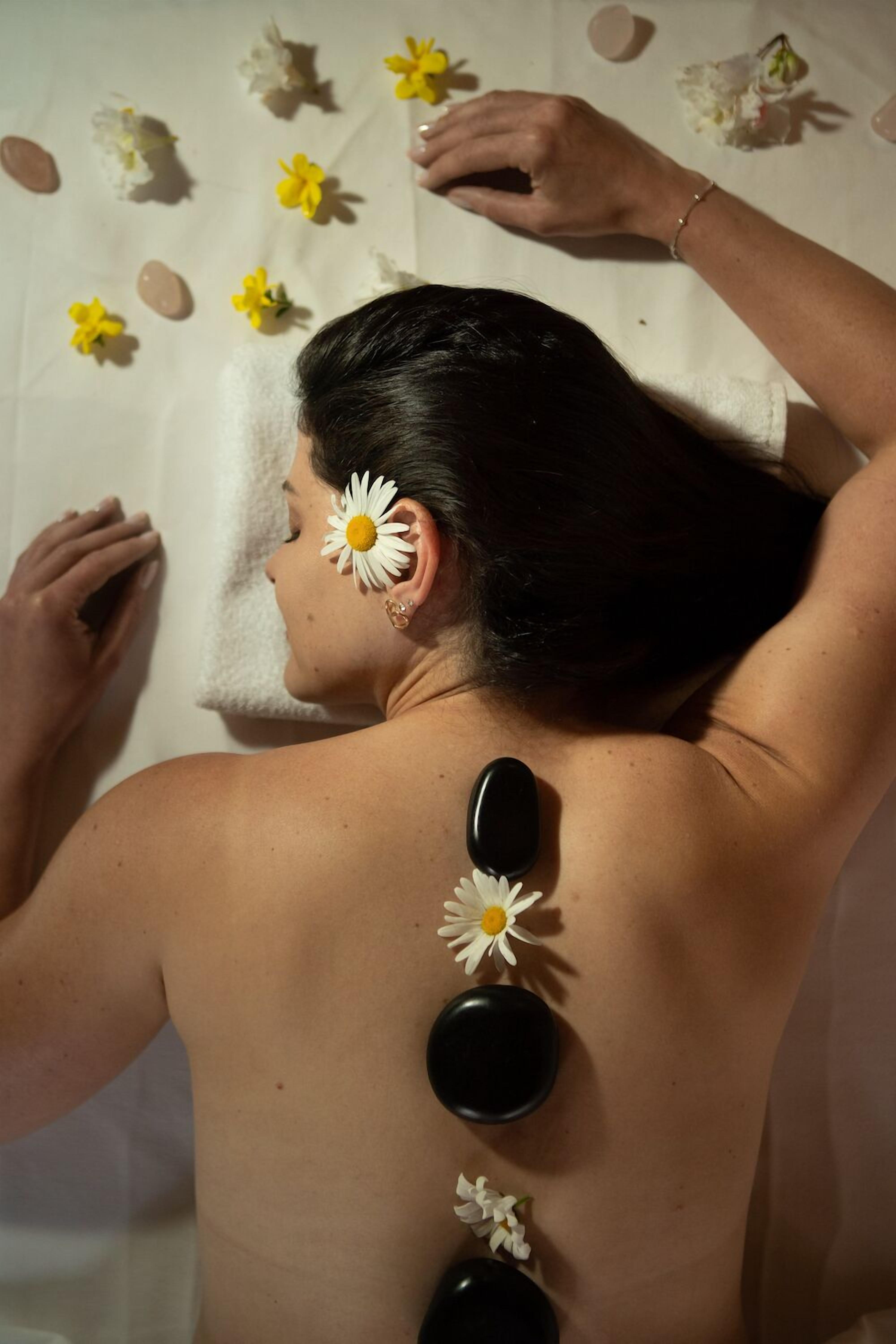 En person modtager en varm steni massage med blomster på ryggen.