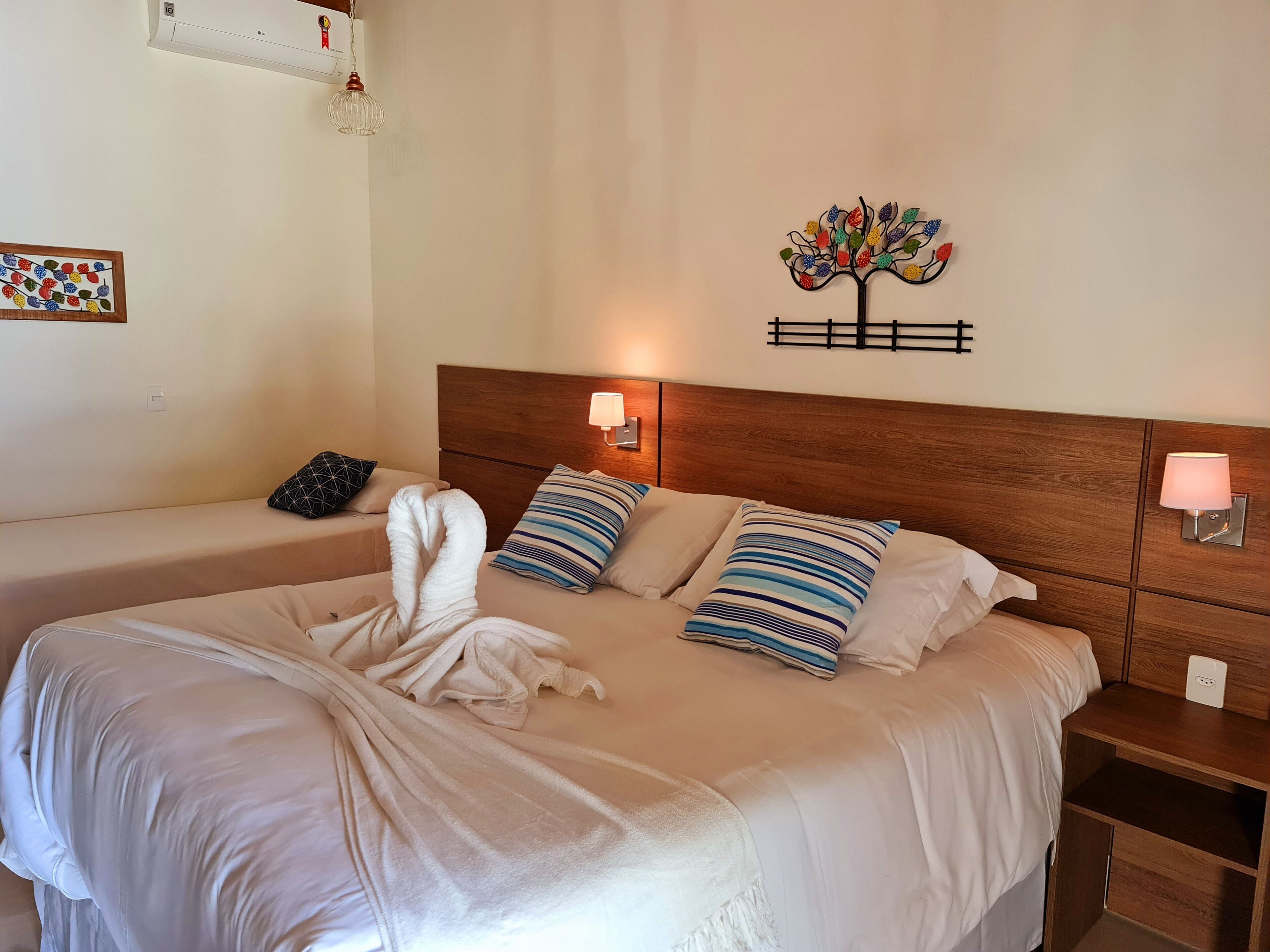 A hotel room with a large bed, two bedside tables, a wooden headboard, and a wall-mounted decorative tree.