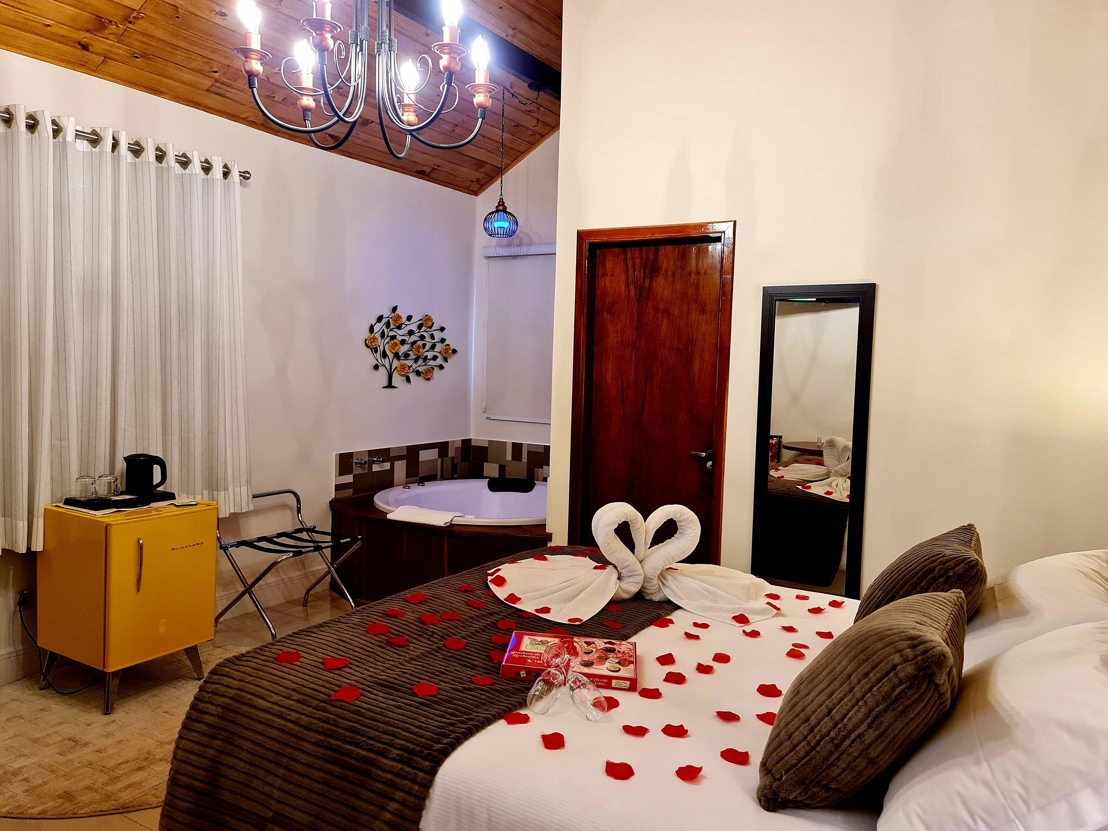 Una habitación de hotel con cama, un aparador de madera, una mesita redonda, un espejo y una araña.