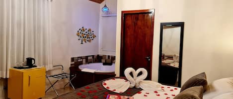 A hotel room with a bed, a wooden cabinet, a small round table, a mirror, and a chandelier.
