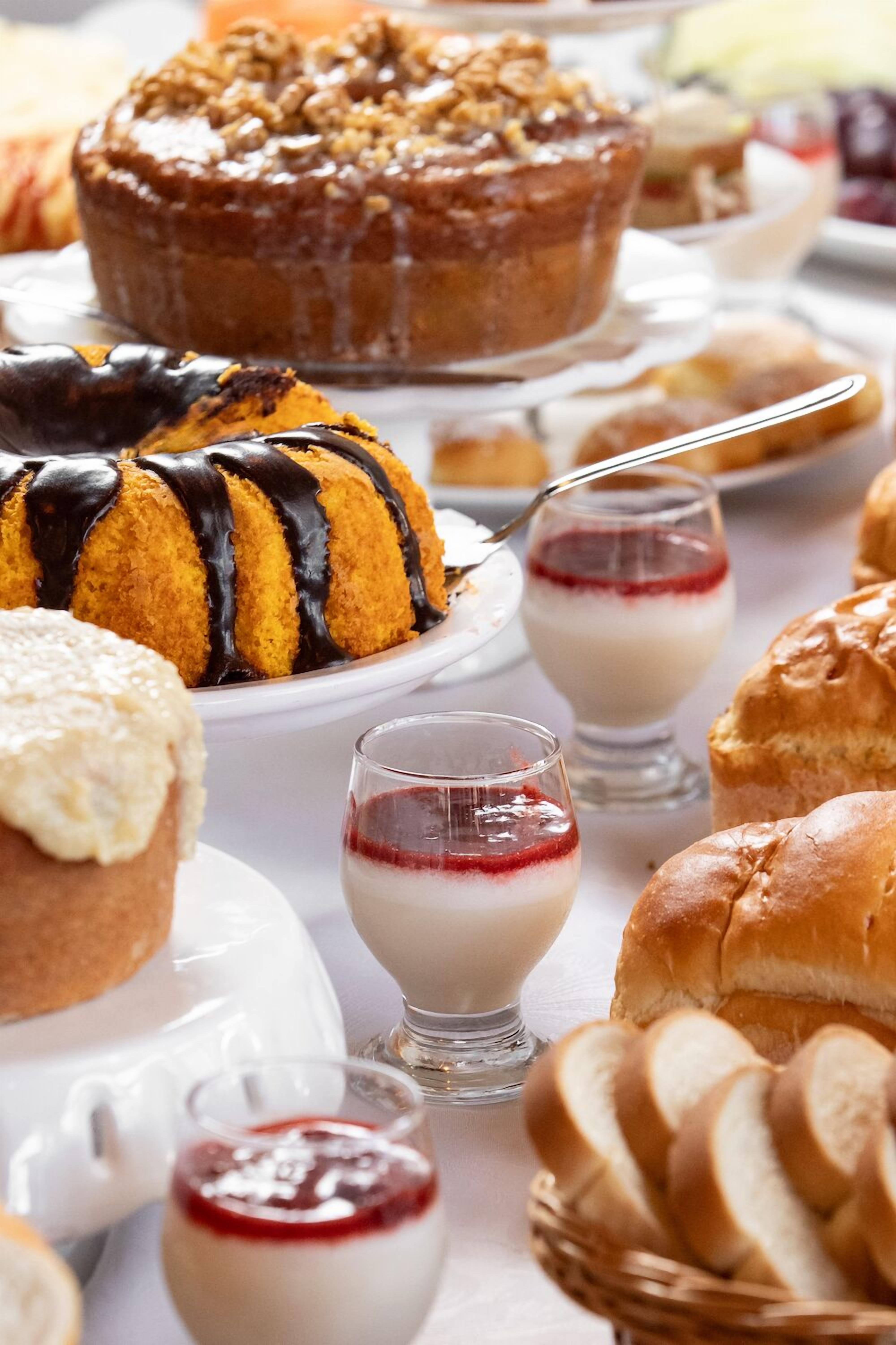 A variety of desserts including a bundt cake, pastries, and small glass dishes with cream and jam.