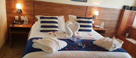 A hotel room with a large bed, two bedside tables, a wooden headboard, and wall art depicting a canal scene.