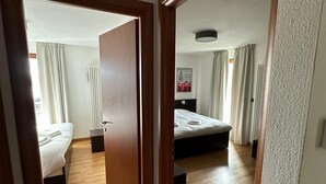 Una habitación de hotel con suelo de madera, dos camas, un radiador y una lámpara en el techo.