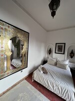 Un dormitorio con un espejo grande y ornamentado, una cama con ropa de cama blanca y una alfombra roja.