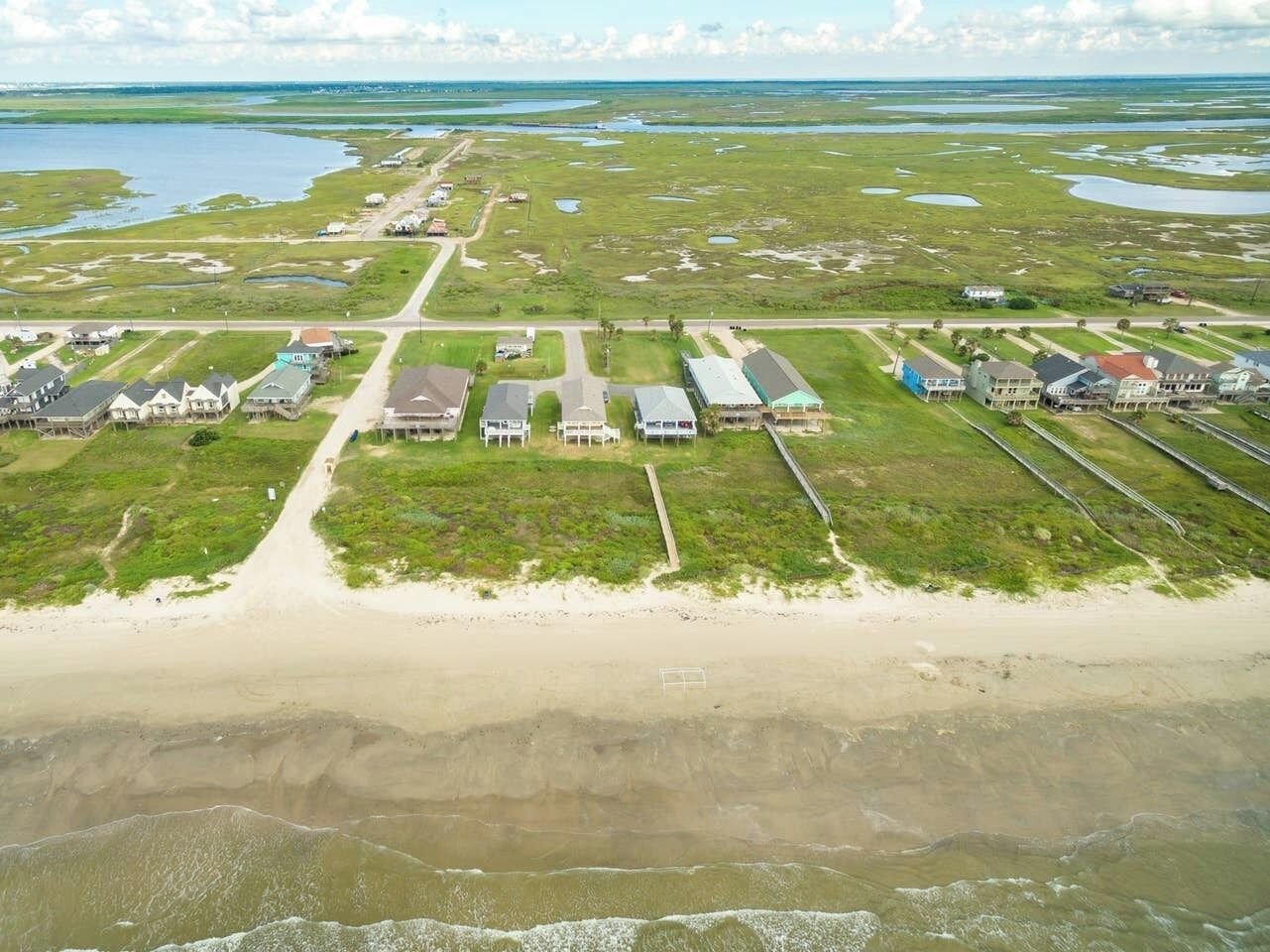 An aerial view of a coastal area with a beach, houses, and a road.