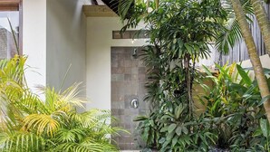 A modern outdoor area with a stone door, lush greenery, and a pebble path. - Villa Tigamangga Central Seminyak Oberoi 10mn walk (Seminyak)