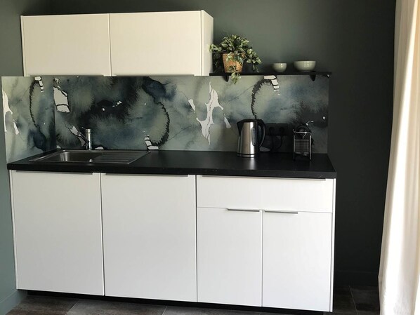 A modern kitchen with a black countertop, white cabinets, and a marble backsplash. - Les Arbres Rouges (Suce-sur-Erdre)