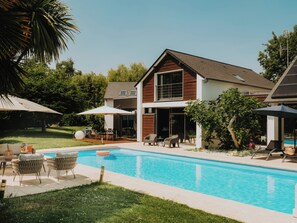 Una casa moderna con piscina, mobiliario exterior y una zona de patio.