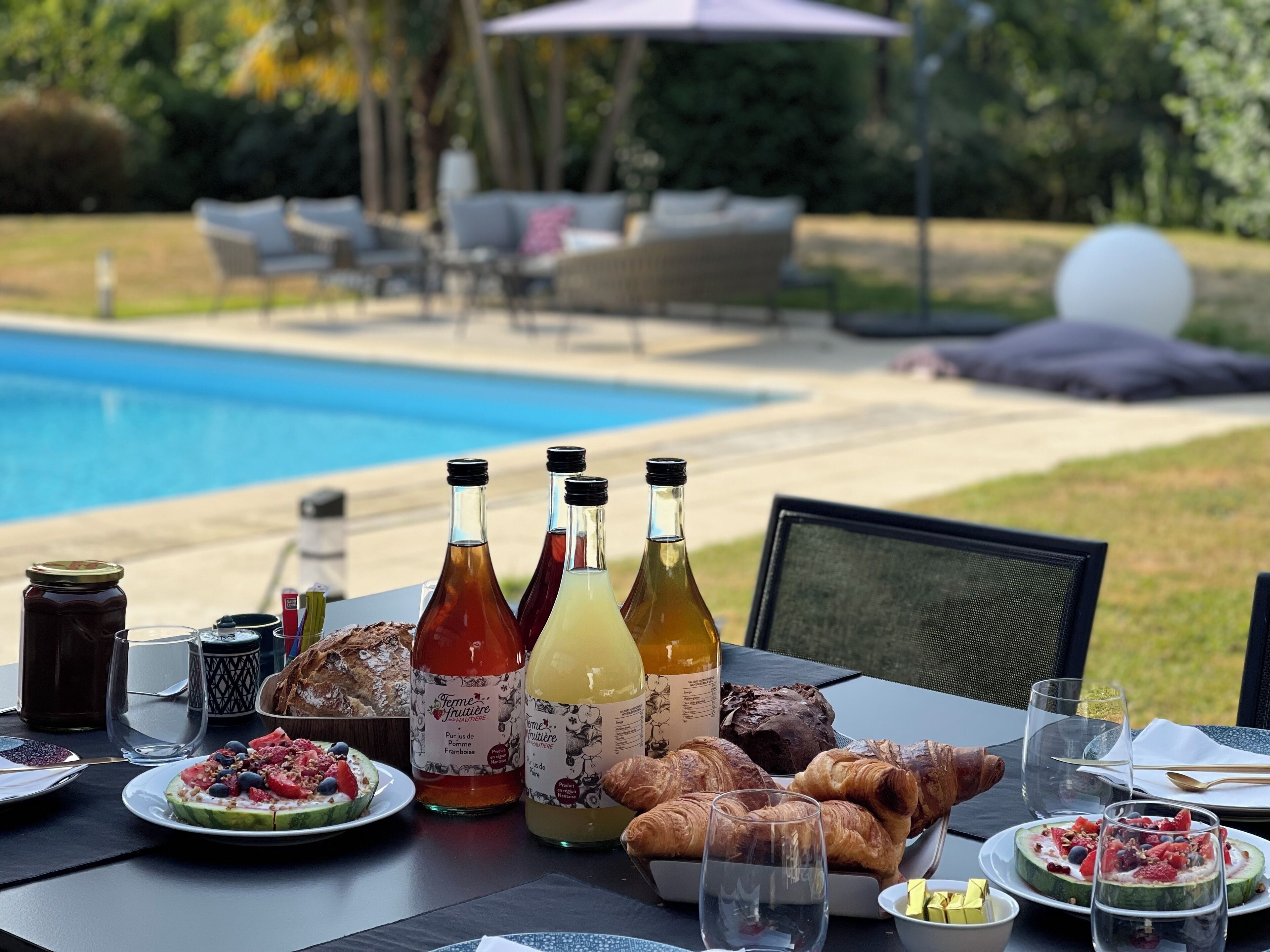 A dining table with food and drinks, a pool in the background, and outdoor furniture.