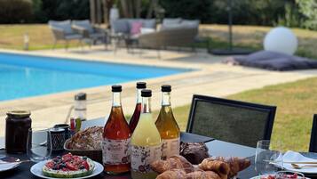 A dining table with food and drinks, a pool in the background, and outdoor furniture.