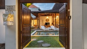 Entrada a una villa con piscina, sillones de descanso y televisor en la sala.