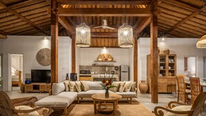 Amplia sala de estar con techo de madera, un conjunto de sofás, una mesa de centro y sillones de mimbre.